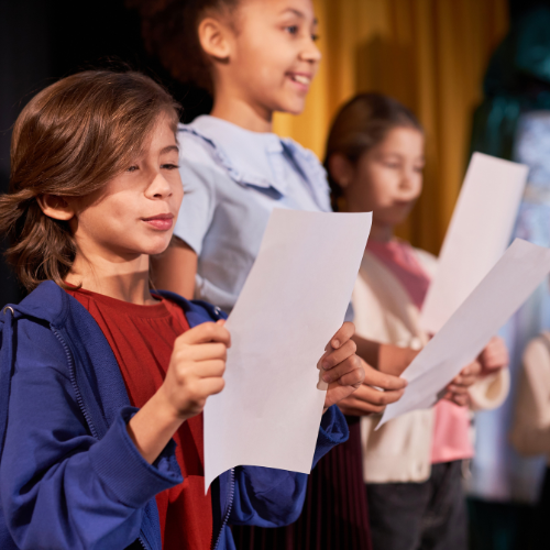 Crianças em aula de teatro, segurando folhas de papel com textos