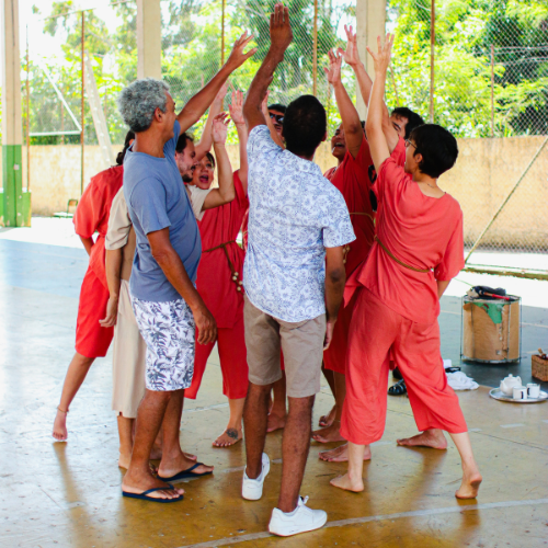 Grupo de adultos em círculo durante oficina de teatro, com os braços levantados
